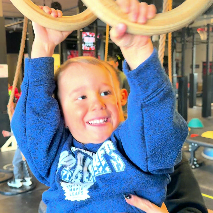 A little ninja grinning as he hangs from the rings